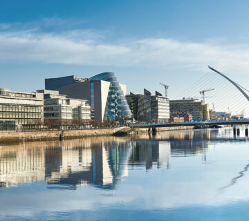 Modern buildings and offices on Liffey river in Dublin on a bright sunny day, bridge on the right is a famous Harp bridge.